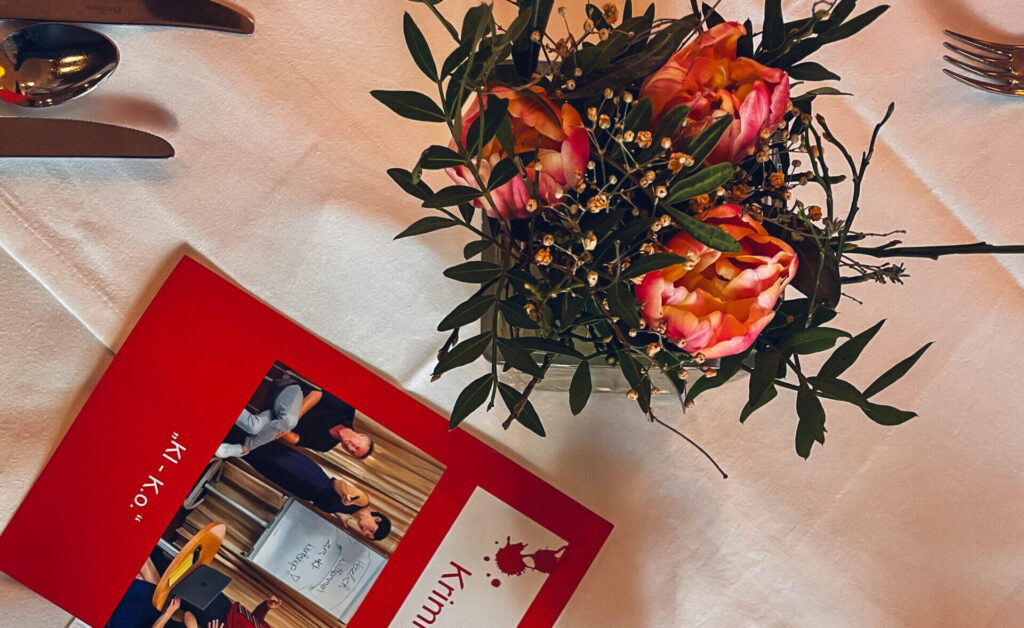 Gedeckter Tisch mit Blumen, einer Kerze und de Menükarte für das Krimidinner