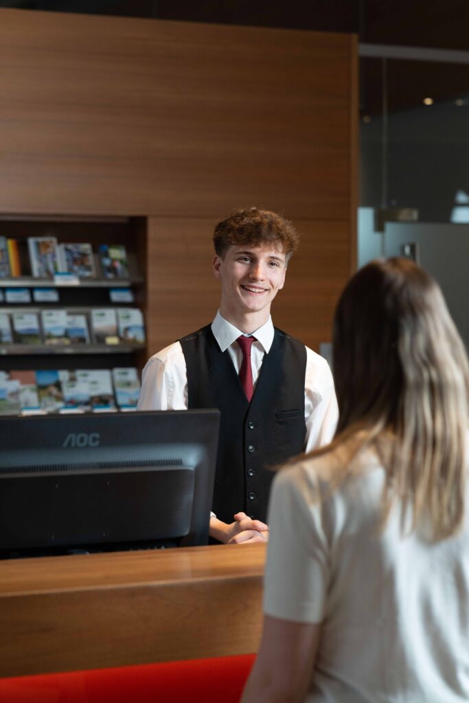 Ein Mitarbeiter erklärt einem Gast gerade etwas an der Rezeption.