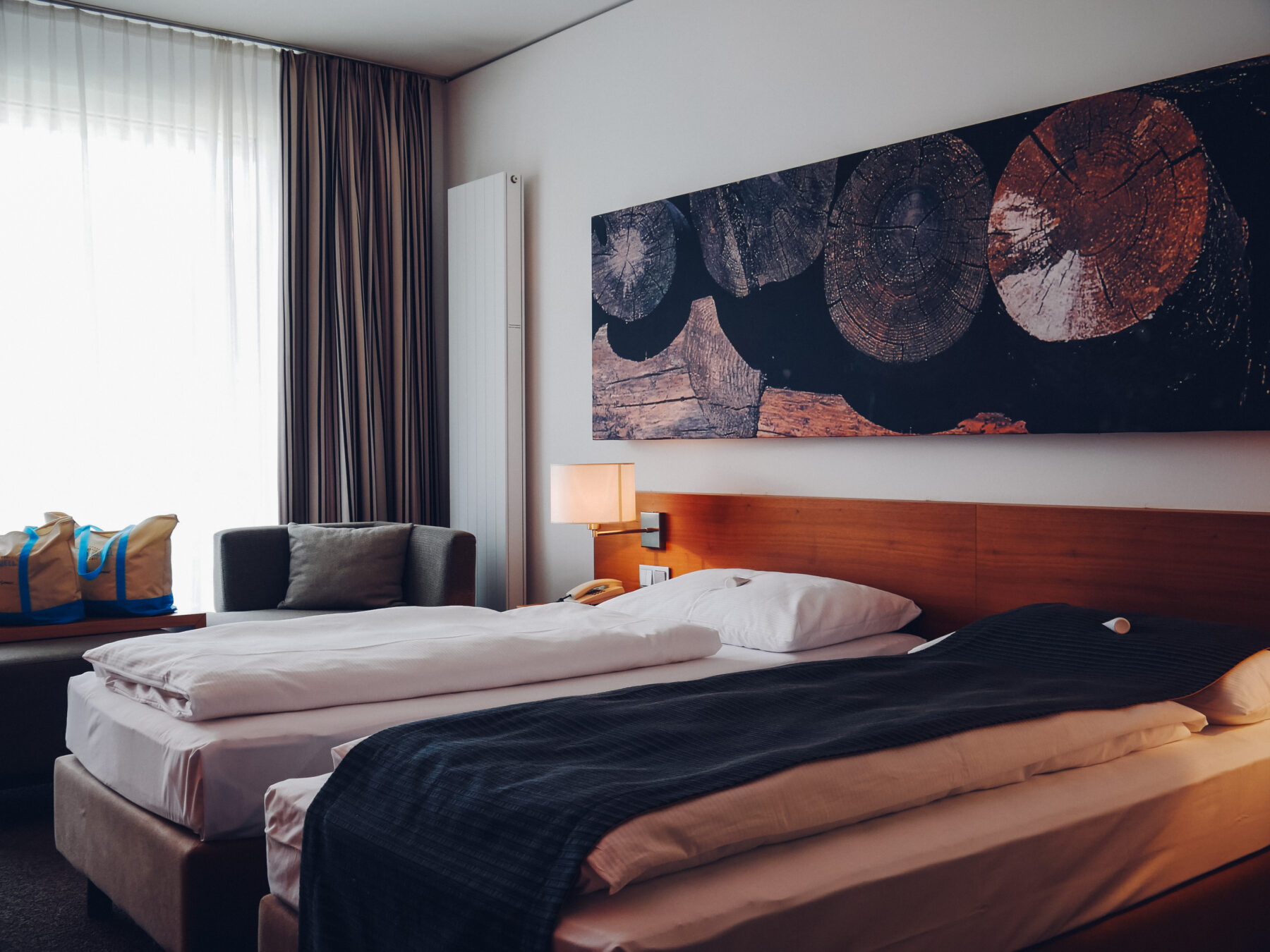 Hotelzimmer mit Doppelbett und auf der Seite stehen zwei Badetaschen und ein Hocker.