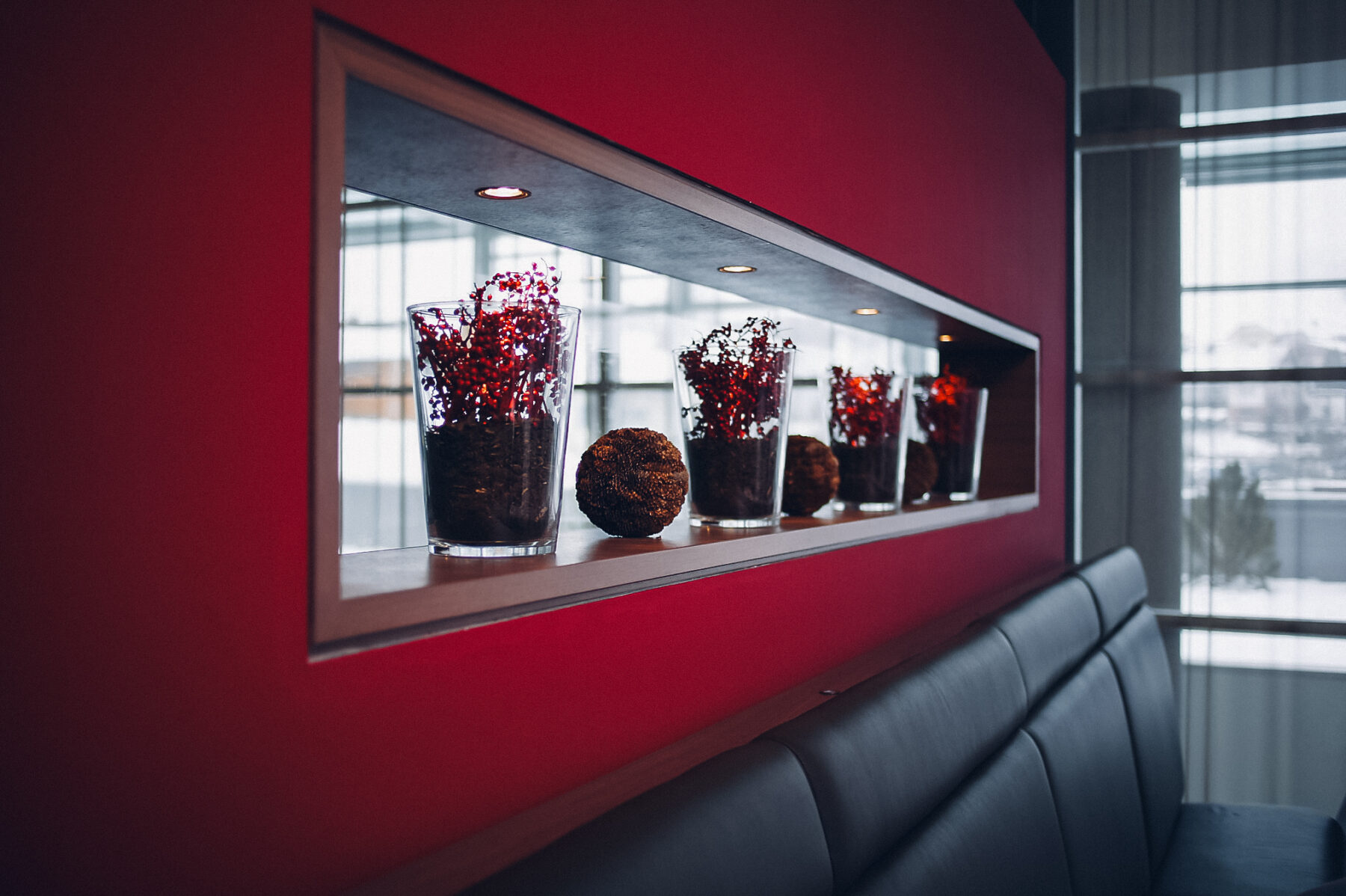 Man sieht eine Sitzbank vom Restaurant und hinterbei eine Wand welche einen rechteckigen Ausschnitt hat, der mit Lichtern und Deko besetzt ist.