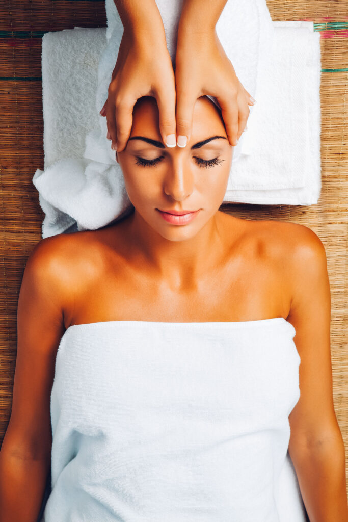 Eine Frau wird am Kopf massiert, sie ist in eine Handtuch eingewickelt.