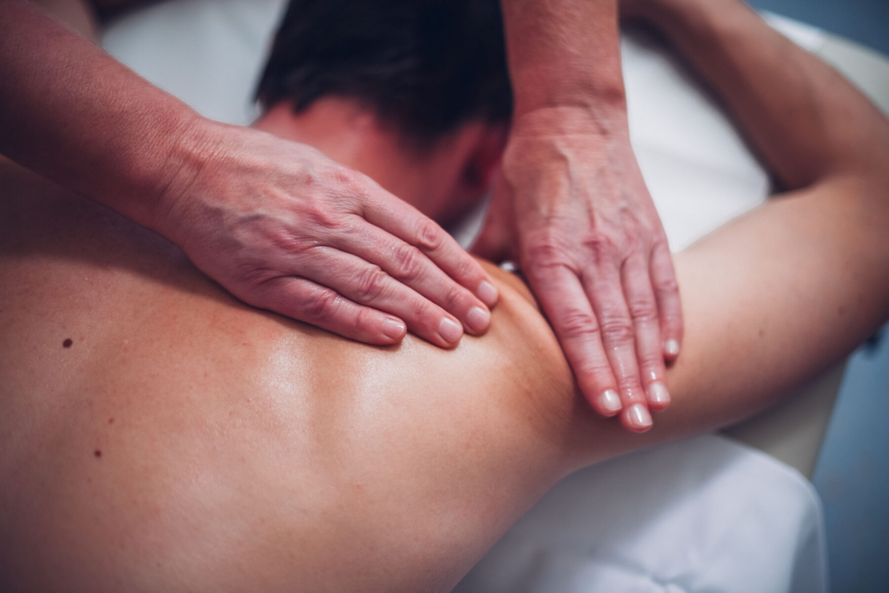 Ein Mann wird auf der rechten Schulter massiert von einem Therapeuten.