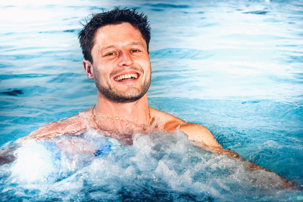 Ein Mann der in einem Becken Einzelunterwasser-Therapie macht mit einem Lächeln.