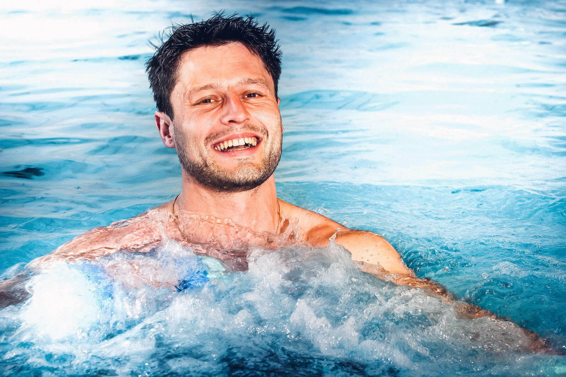 Ein Mann der in einem Becken Einzelunterwasser-Therapie macht mit einem Lächeln.
