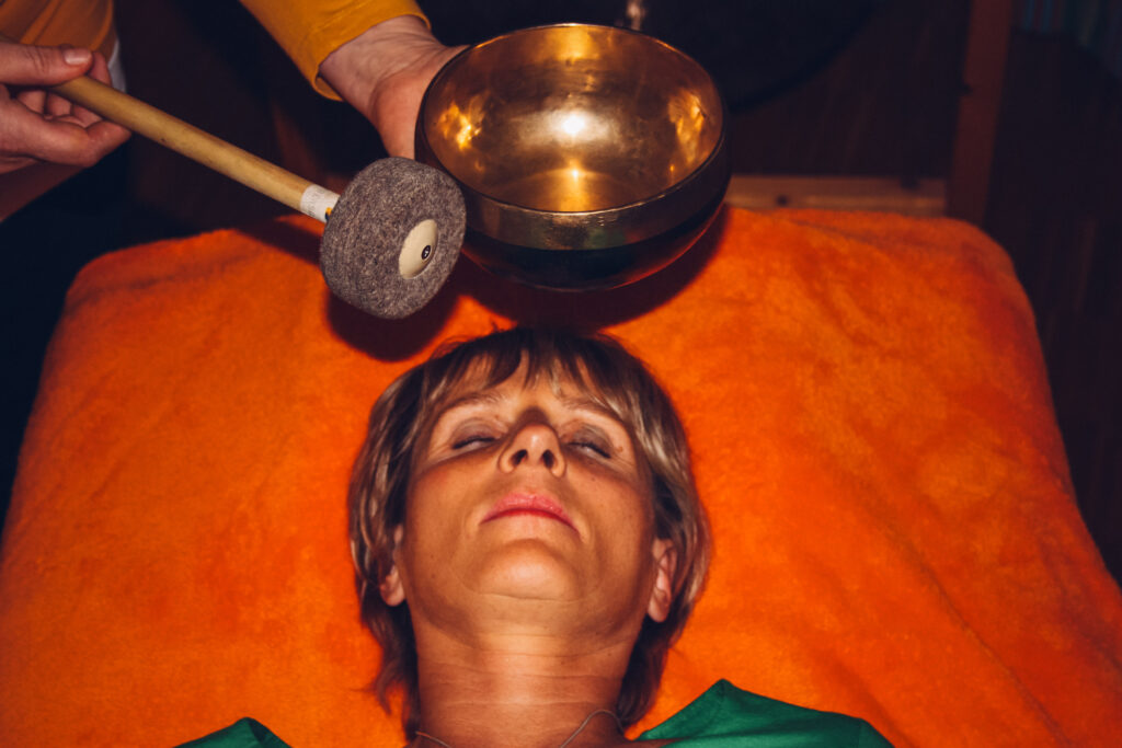 Frau liegt entspannt, über ihrem Kopf wird eine Klangschale für Klangtherapie gehalten.