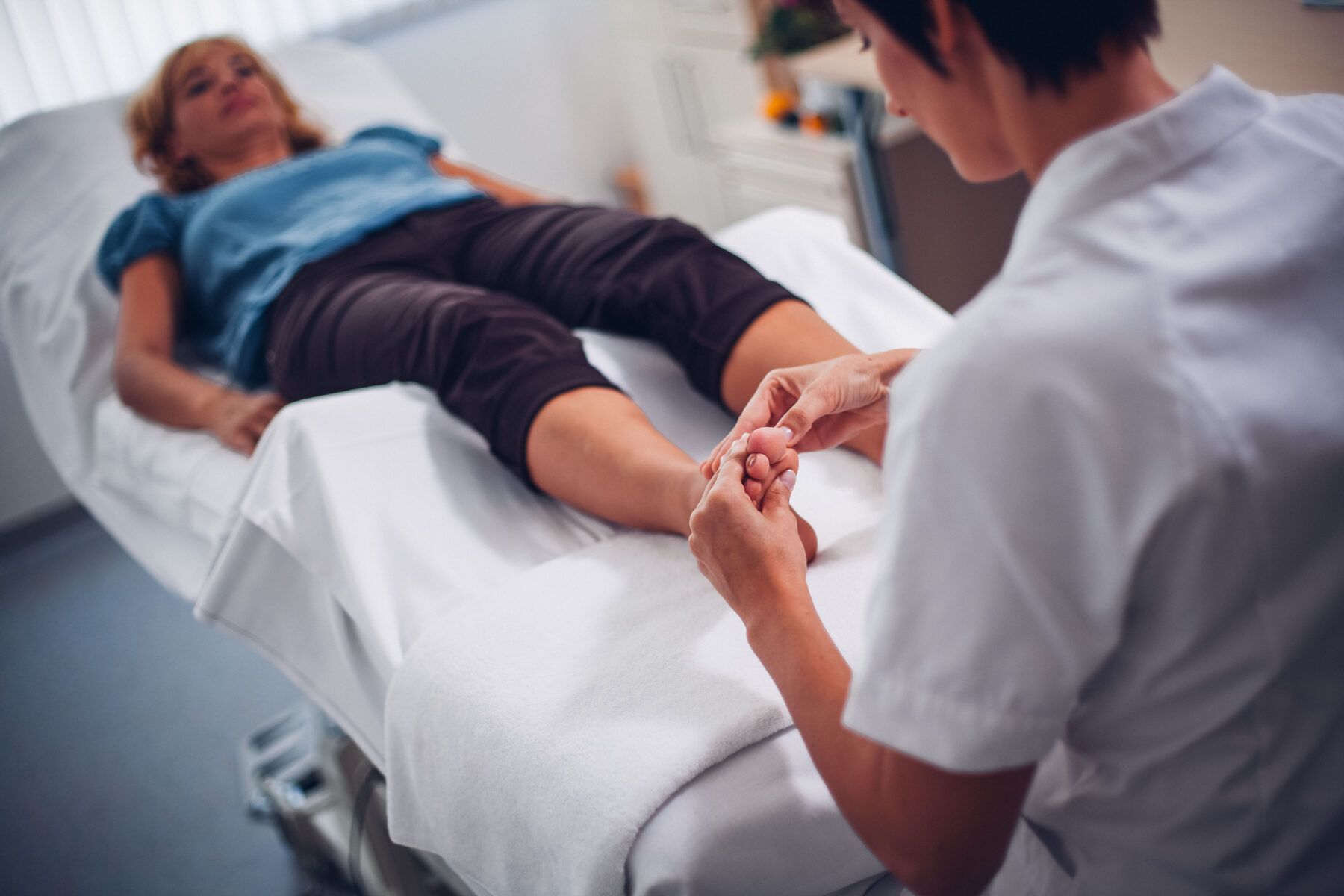 Eine Frau massiert einer jungen Dame die Füße während sie auf der Liege liegt.