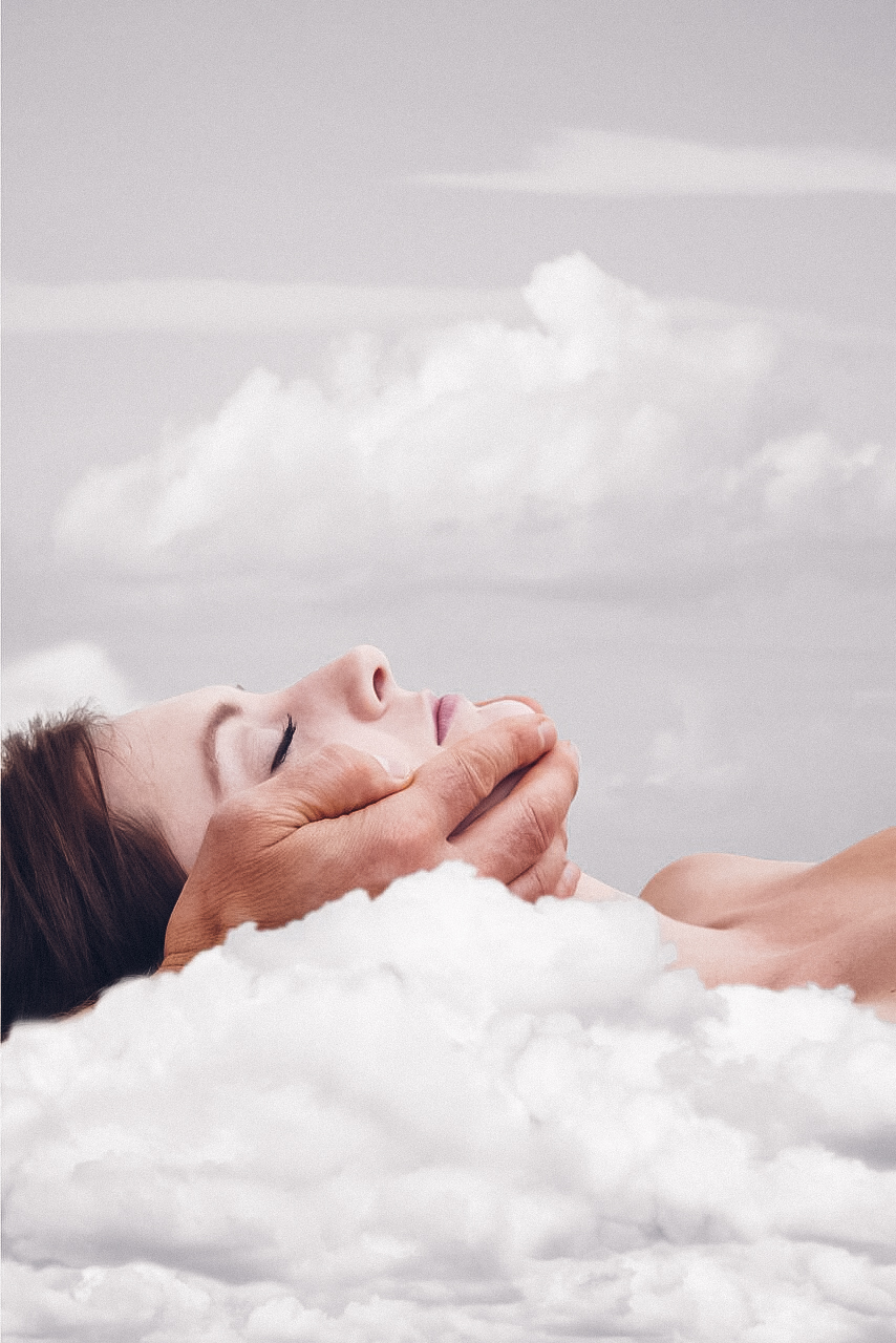 Eine Frau liegt entspannt in Wolken, eine Hand hält ihr Gesicht sanft.
