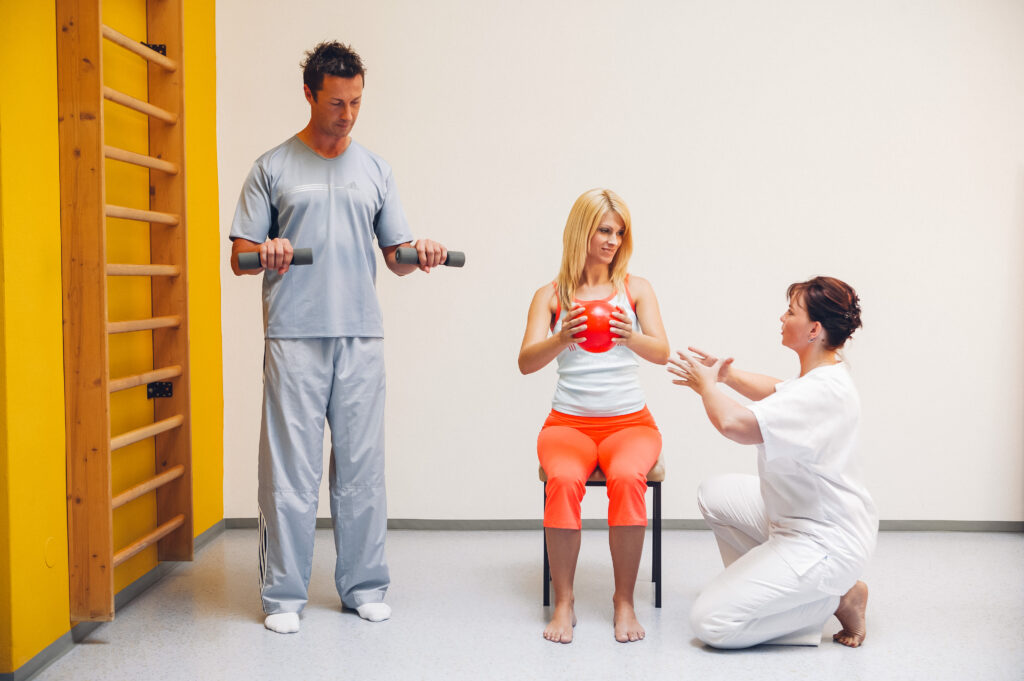 Physiotherapeutin gibt Anweisungen, zwei Patienten machen Übungen für Kraft und Koordination.