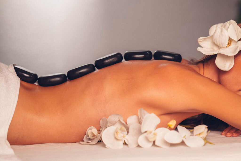 Eine Frau die geschmückt mit Blumen ist hat heiße Steine entlang der Wirbelsäule.