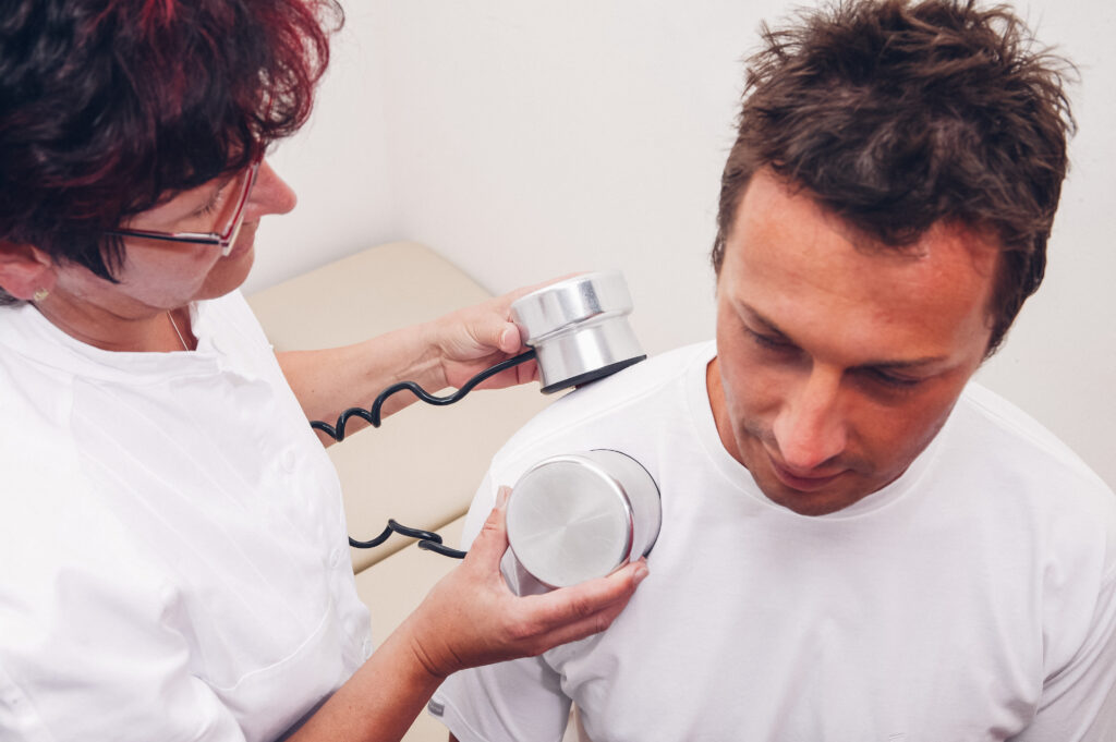 Auf dem Bild behandelt eine Therapeutin einen Mann mit einem Ultraschallgerät an der Schulter.