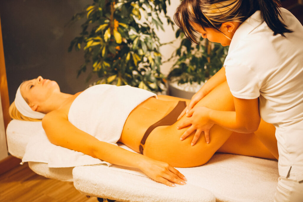 Eine Kosmetikerin massiert die Beine einer jungen Frau die auf einer Massageliege liegt.