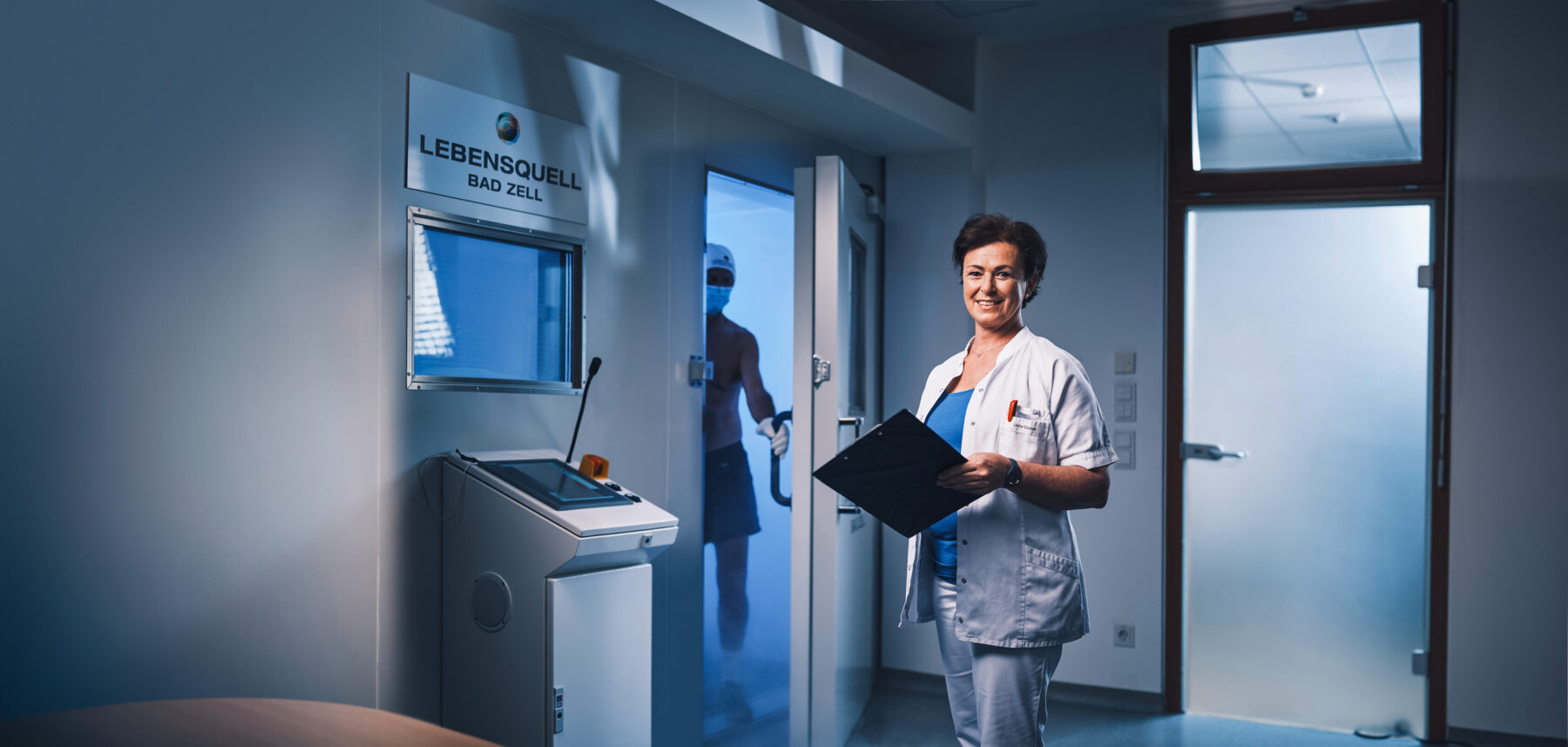 Eine Therapeuten, im Hintergrund die Kältekammer, wo gerade ein Patient rausgeht