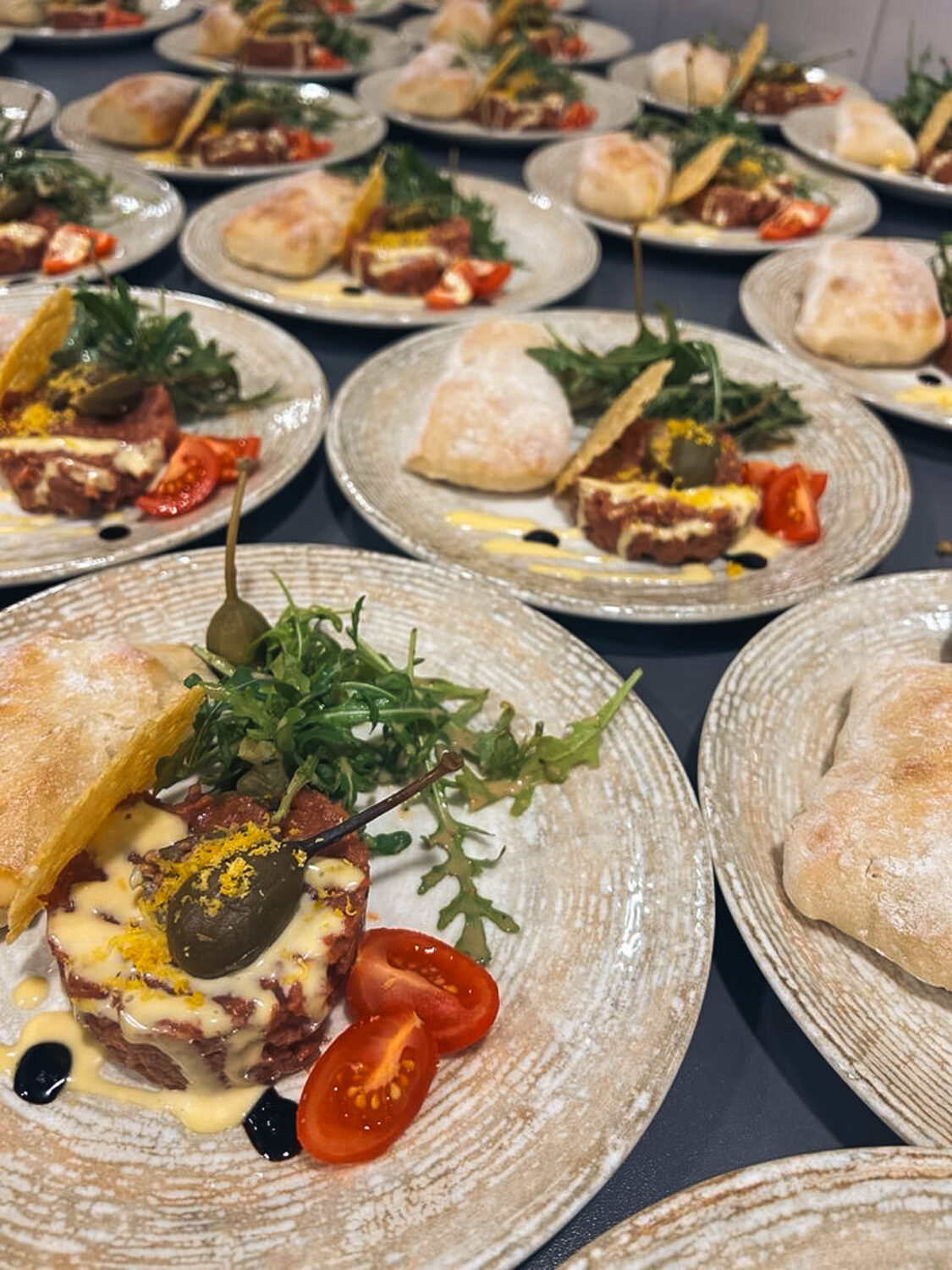 Man sieht viele angerichtete Teller mit Capriccio, Rucola, Tomaten und einem Stück Gebäck.