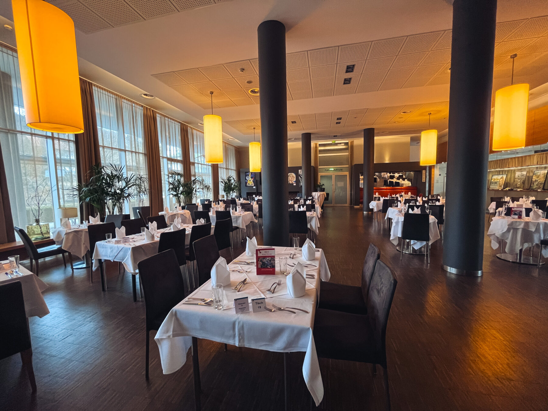 Festlich gedeckte Tische in einem Restaurant mit großen Fenstern und Hängeleuchten