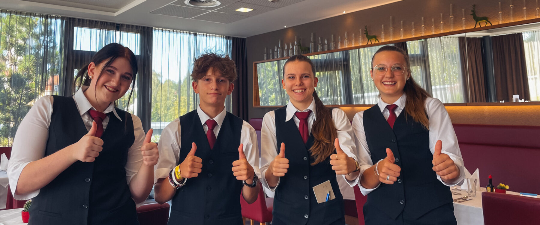 Vier Lehrlinge, welche lachen und Daumen nach oben zeigen. Im Hintergrund ist das Restaurant erkennbar.