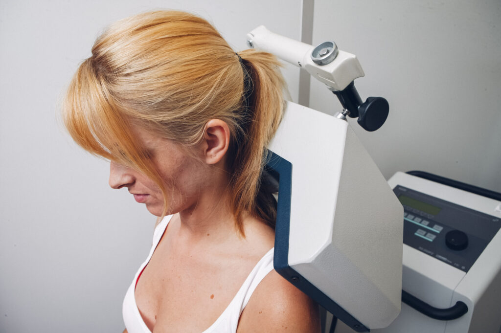 Die Frau erhält eine physiotherapeutische Behandlung mit einem Ultraschallgerät, das auf ihren Nackenbereich gerichtet ist.