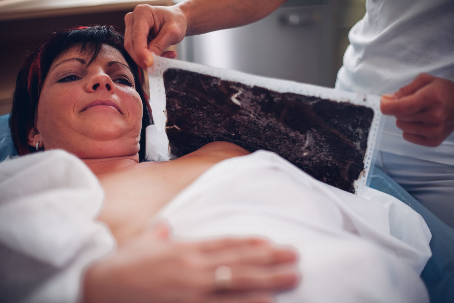 Die Therapeutin legt die Moor-Packung auf die Schulter der liegenden Frau.