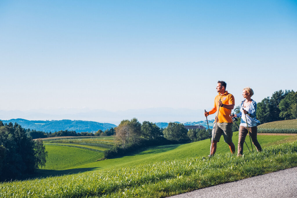 Eine Frau und ein Mann die im Mühlviertel Wandern gehen mit Wanderstöcken bei guten Wetter mit schöner Natur um Ihnen herum.