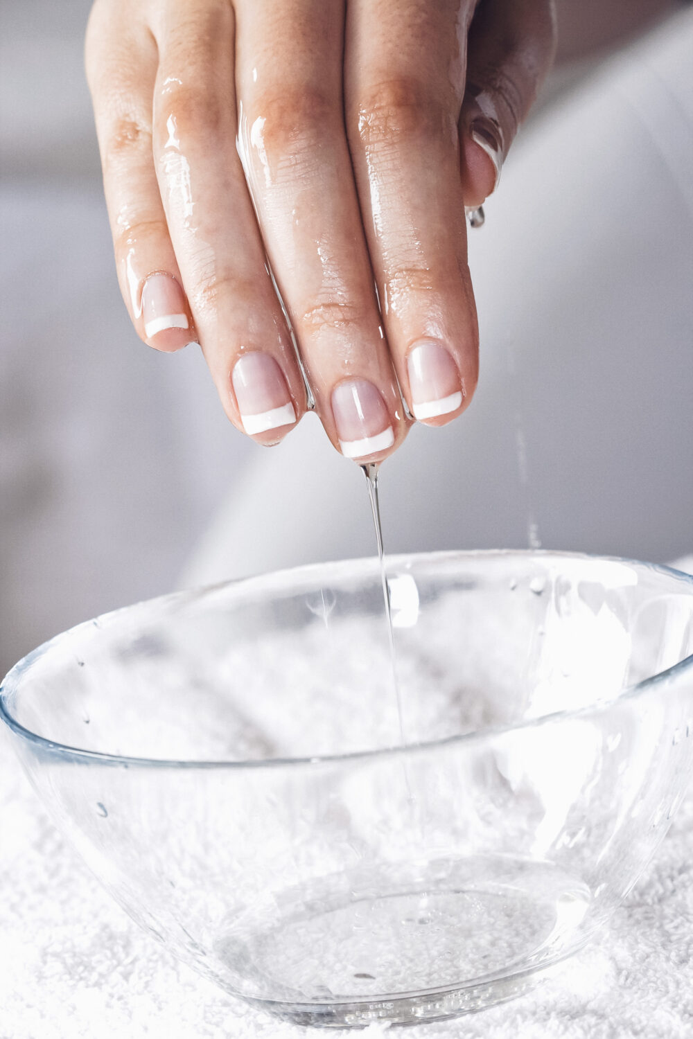 Eine Hand mit French Maniküre taucht in eine Glasschüssel mit Wasser.