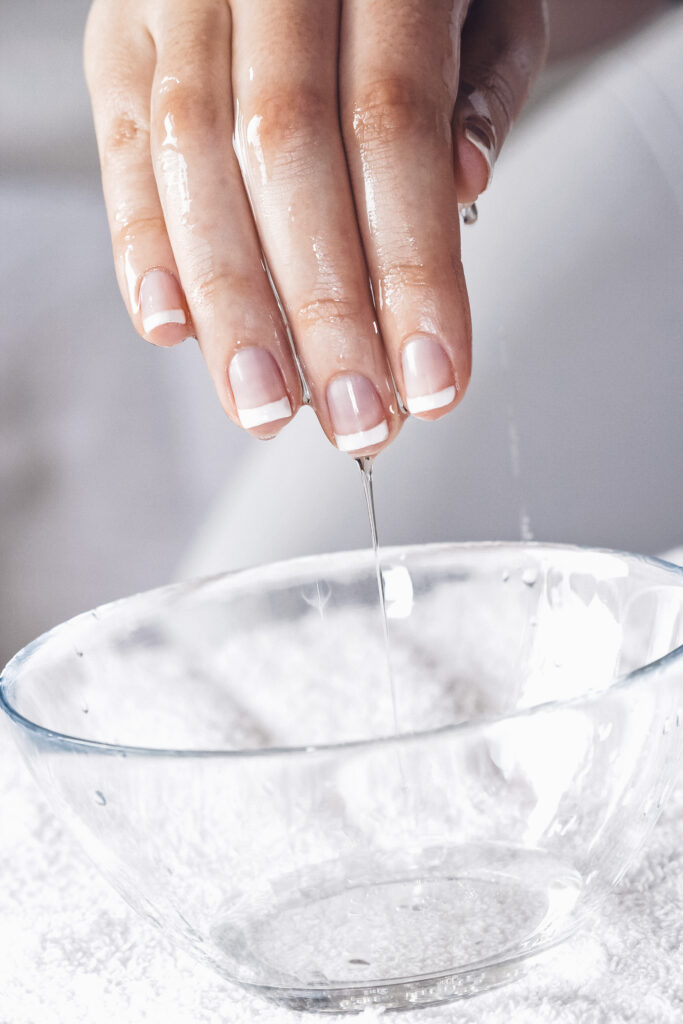 Eine Hand mit French Maniküre taucht in eine Glasschüssel mit Wasser.