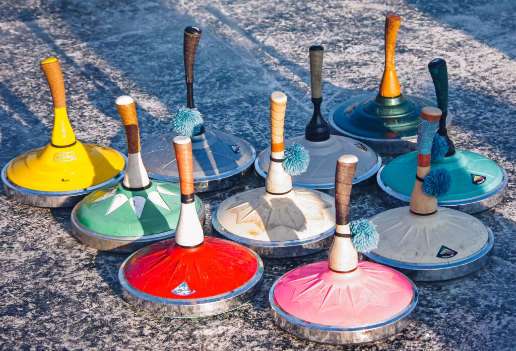 Man sieht mehrere bunte Eisstöcke auf einer Eisstockbahn nebeneinander stehen.