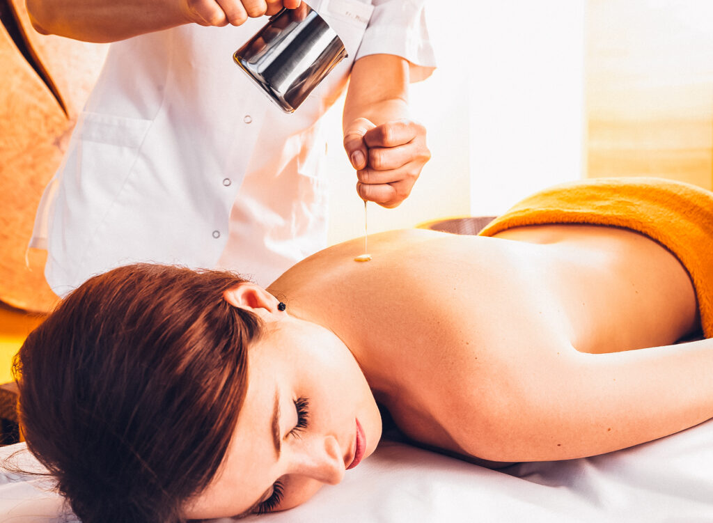 Eine Frau liegt entspannt auf einer Massageliege, während ihr warmes Öl auf den Rücken gegossen wird.