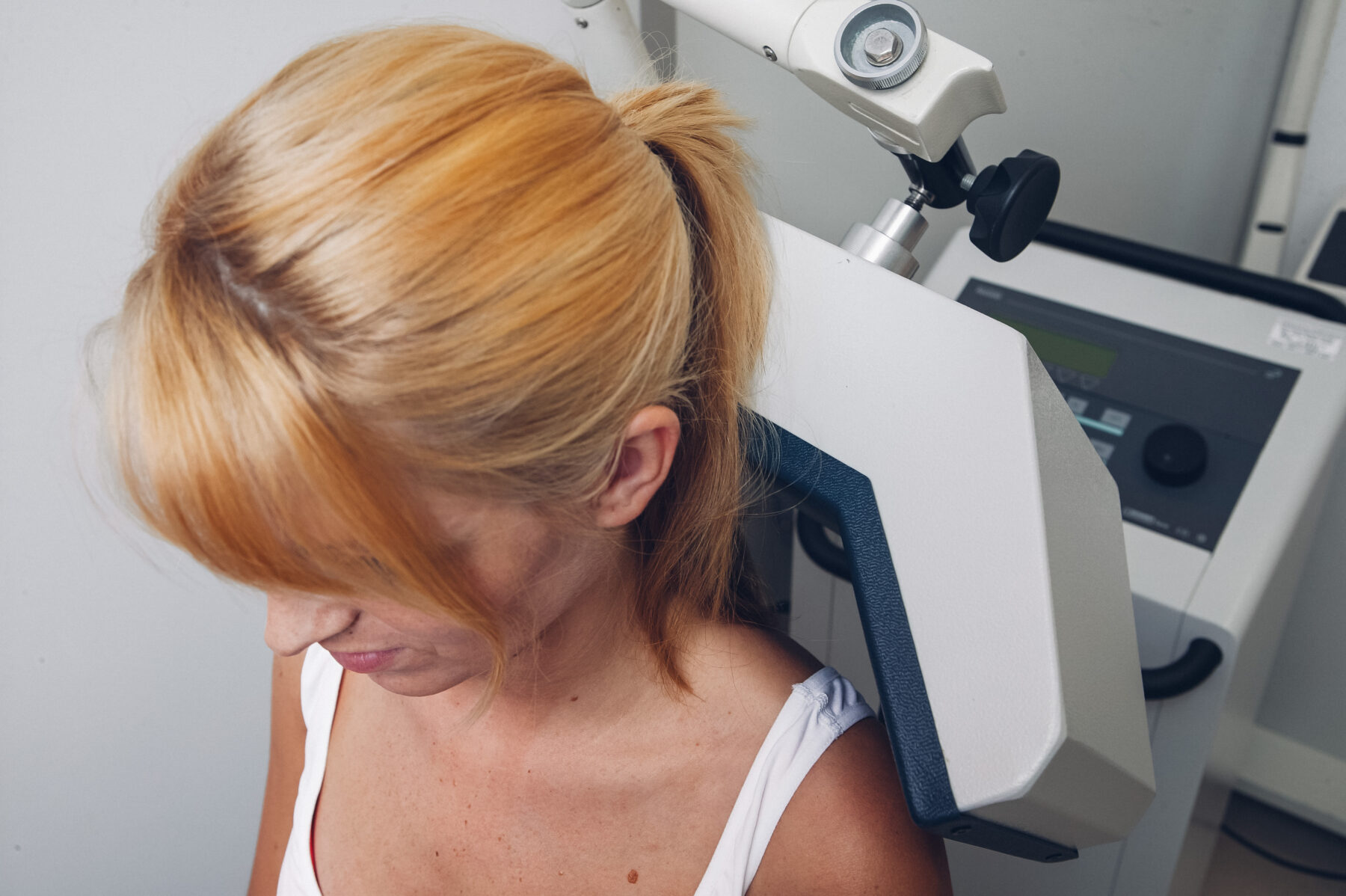 Die Frau erhält eine physiotherapeutische Behandlung mit einem Ultraschallgerät, das auf ihren Nackenbereich gerichtet ist.