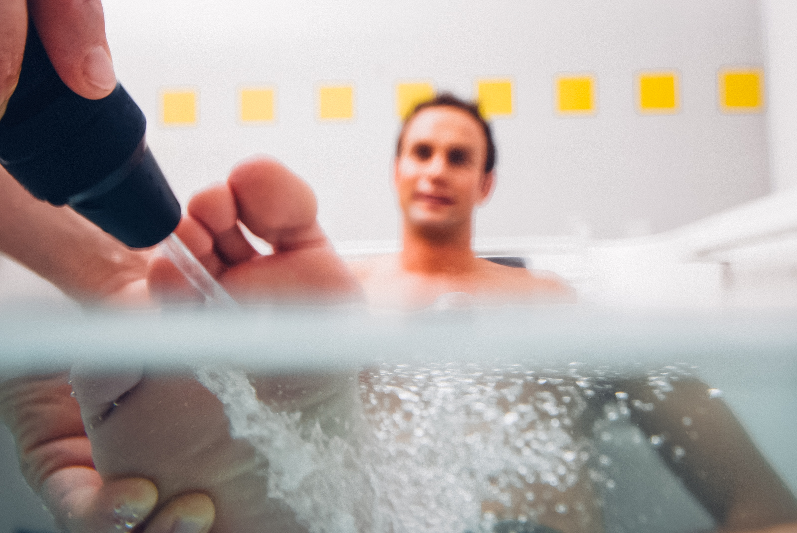 Ein Mann der in einer Wanne sitz wir mit einem Wasserstrahl auf den Füßen massiert.
