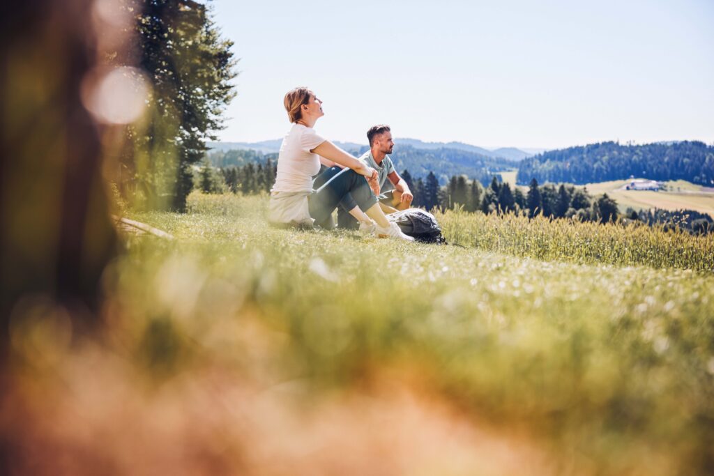 Man sieht zwei Personen in der Wiese sitzen und die Sonne genießen.