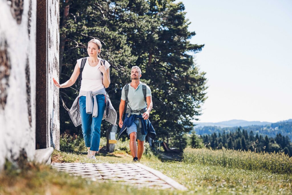 Man sieht zwei Personen beim Wandern, welche gerade zum Eingang einer Kapelle kommen.