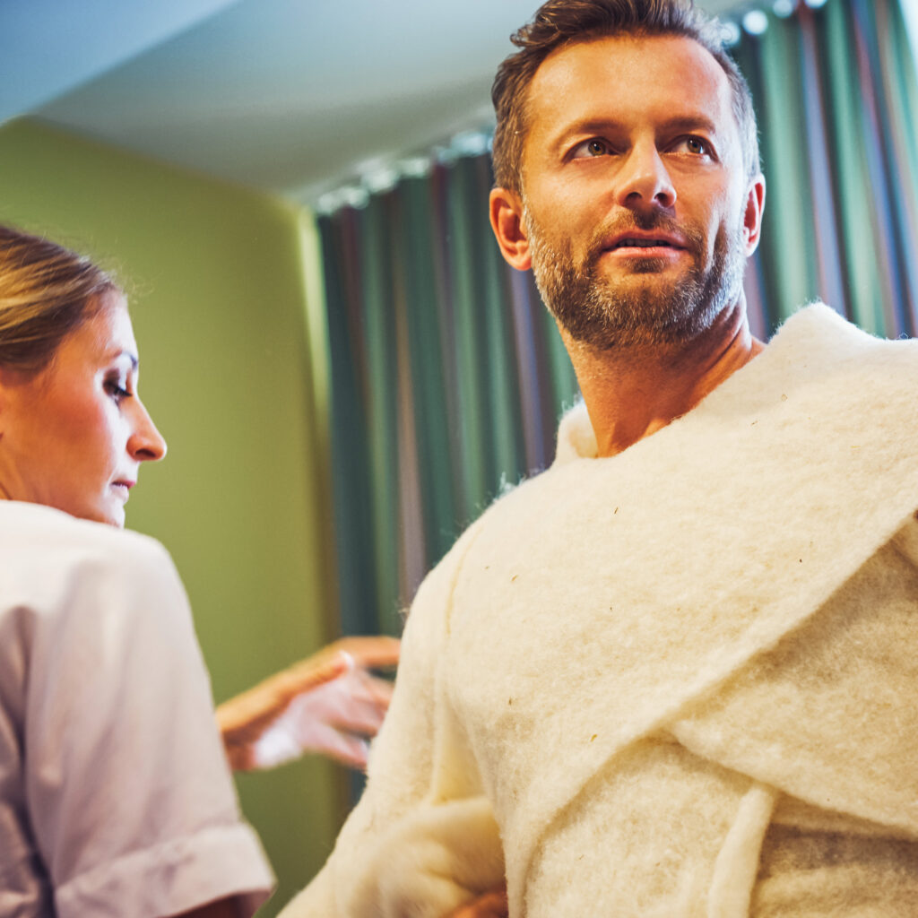 Eine Kosmetikerin wickelt einen Mann in Schafswolle ein.