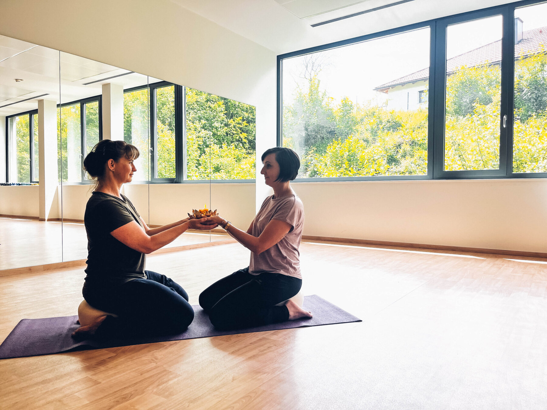 Zwei Frauen die in einem hellen Raum gemeinsam Yoga auf einer Gymnastikmatte machen.