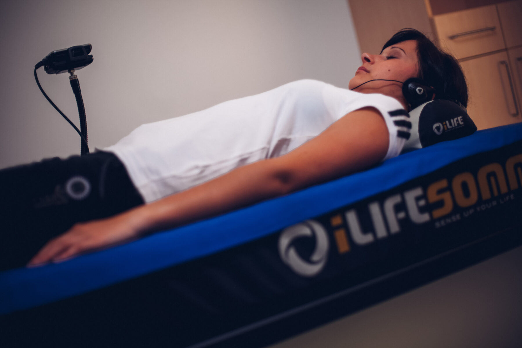 Eine Frau die aufeiner iLife-SOMM-Liege liegt mit Polster und Kopfhörer auf den Kopf hat.